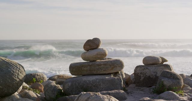 Balanced rock cairn standing on ocean shore during sunset with waves in the background. Ideal for promoting mindfulness, meditation, and relaxation. Suitable for nature themes, wellness blogs, and tranquility-focused advertisements.