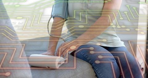 Woman measuring blood pressure at home with digital monitor and circuitry overlay