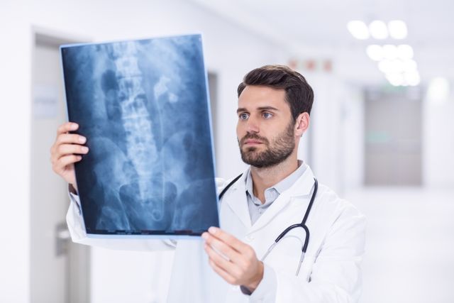 Depicts a male doctor examining an x-ray in a modern clinic, showcasing medical expertise and healthcare environment. Useful for medical articles, healthcare websites, hospital brochures, and educational materials on diagnostics and radiology.