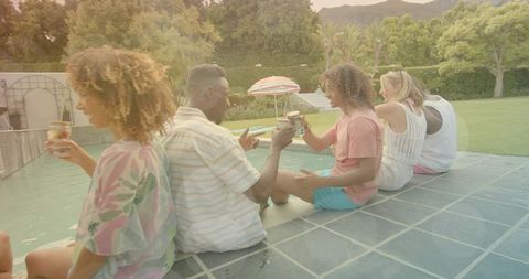 Friends relaxing at backyard pool, clinking drinks and chatting, summer social gathering