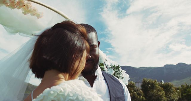 Couple embracing at outdoor wedding ceremony with mountains in the background, symbolizing love and romance. Suitable for wedding themes, promotions for wedding planning services, ads for bridal attire, or articles about outdoor weddings.