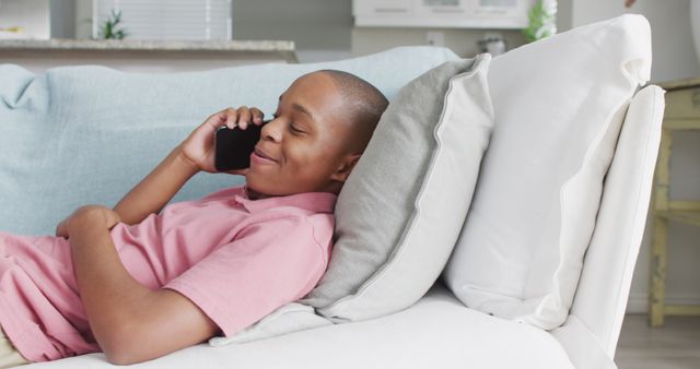 Teenage boy lying on a couch while talking on his phone in a casual and comfortable setting at home. Ideal for depicting leisure time, home life, casual communication, and modern technology use.