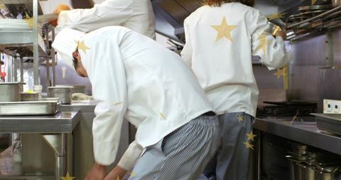 Chefs reaching for pan in busy professional kitchen during service rush