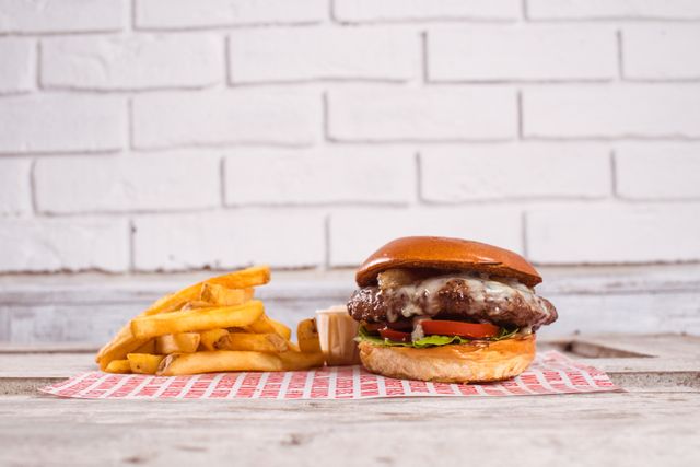 Illustrates a mouth-watering cheeseburger paired with crispy fries on wooden table in front of brick wall. Ideal for advertisements, restaurant menus, food blog posts, social media promotions, and culinary websites.