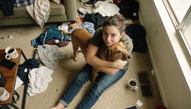 Woman hugging dog on floor in cluttered living room, cozy candid home moment