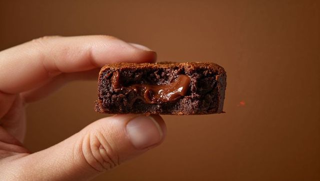 Hand Holding Gooey Chocolate Brownie Square with Molten Center, Close-up Food Detail