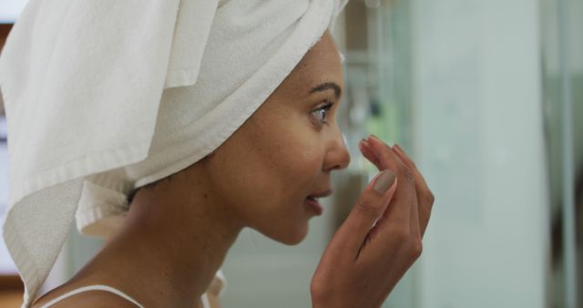 Biracial woman wearing towel on head applying cream on her face - Download Free Stock Photos Pikwizard.com