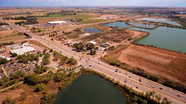 This image captures an aerial view of a countryside intersection surrounded by scenic lakes, farmland, and infrastructure. Ideal for use in road development campaigns, rural tourism promotions, and environmental studies.
