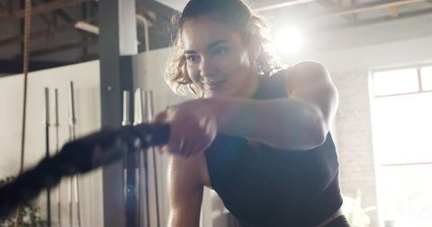 Energetic woman engaged in battle rope workout at gym