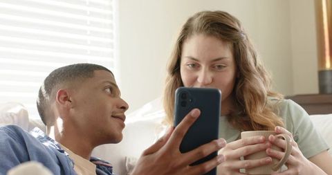 Couple sharing cozy minimalist morning on couch showing phone and holding mug