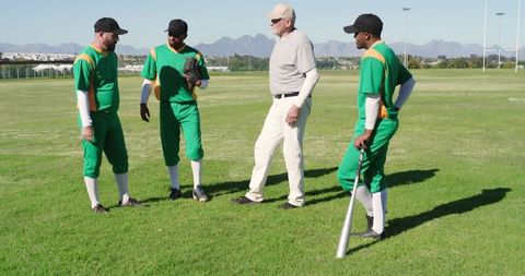 Senior coach leading baseball players in green uniforms during outdoor practice
