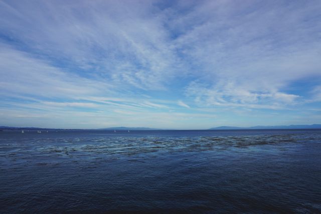 Calm ocean view under expansive blue sky with scattered clouds. Ideal for travel blogs, relaxation and meditation materials, or nature-themed websites. Suitable for backgrounds, desktop wallpapers, or promotional content depicting tranquility and serenity.