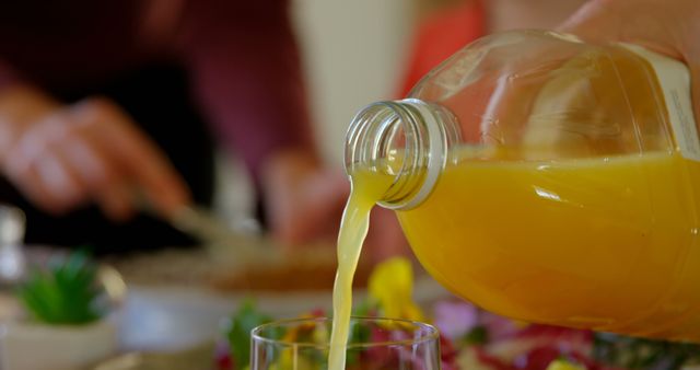 Close-up capturing hand pouring fresh orange juice into glass during breakfast. Ideal for illustrating morning routines, healthy eating, or kitchen activities. Useful for food and drink blogs, breakfast recipes, or health and wellness content.