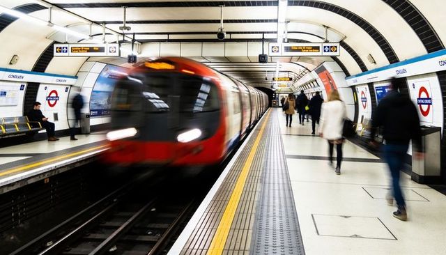 Red london underground train blurring past busy platform during rush hour commute