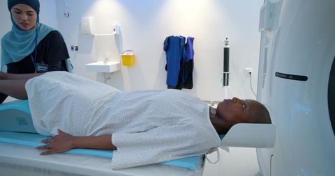 Male patient undergoing ct scan with hijab-clad technologist in bright radiology suite