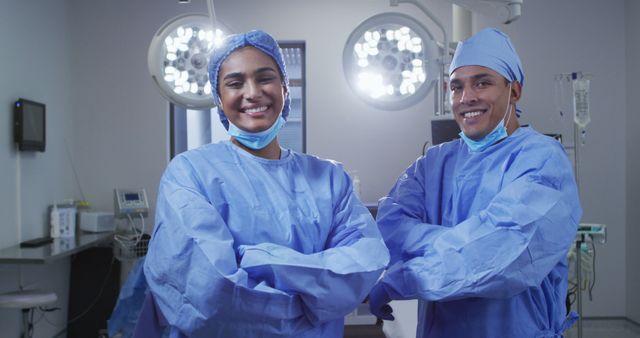Portrait of diverse male and female surgeon wearing lowered face masks smiling in operating theatre. medicine, health and healthcare services during covid 19 coronavirus pandemic.