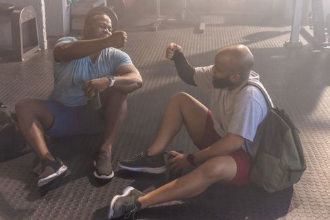 African american men sitting on gym floor fist bumping post-workout showing camaraderie