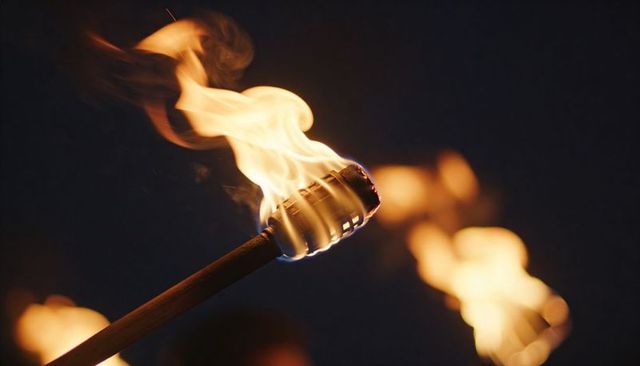 Burning handheld torch with metal-wrapped head casting warm flame and bokeh
