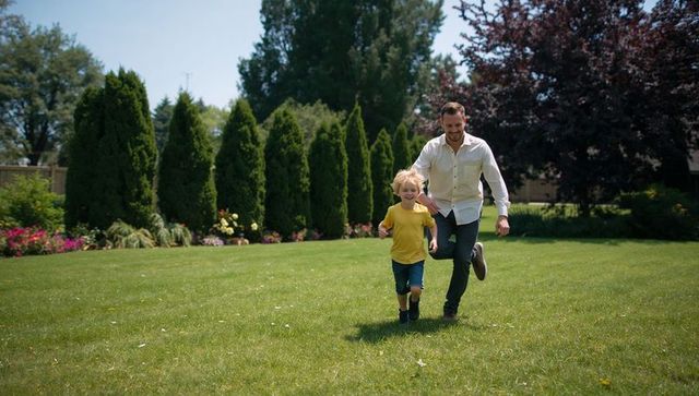 Father and Son Running Across Sunny Backyard Lawn During Weekend Play and Family Bonding