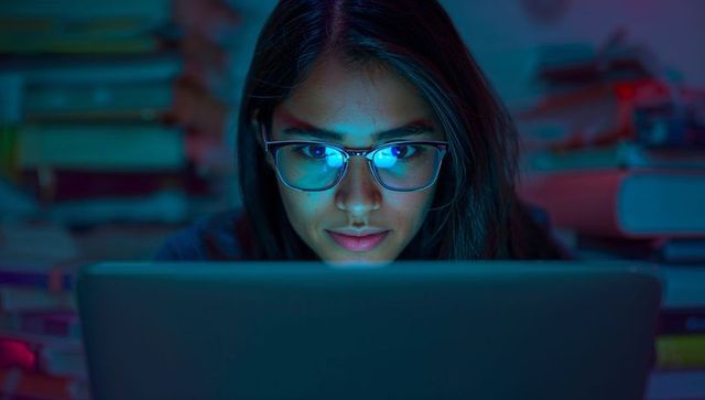 Focused student with glasses studying at night by laptop