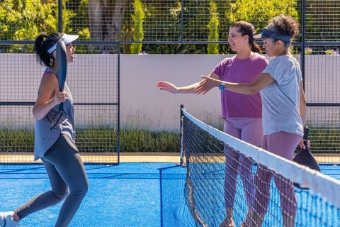 Diverse women shaking hands across padel net on vivid blue court friendly match moment