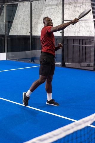 Playing padel on indoor blue court, athlete swinging racket in dynamic action