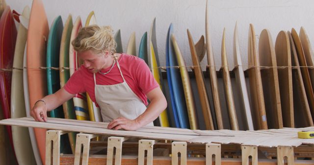 Craftsman working on shaping a surfboard in rural workshop filled with various surfboards hanging on wall. Surfboard making involves precision, skill and creativity. Use for themes related to craftsmanship, surfing culture, woodworking, handmade artisan products, surfing industry.