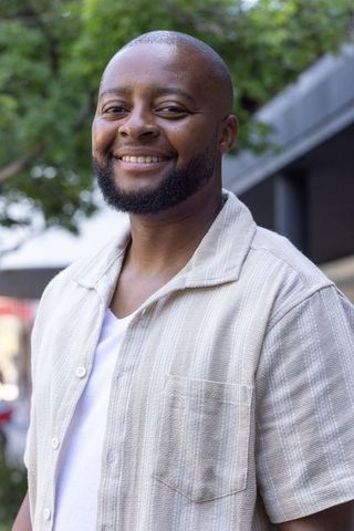 Confident smiling african man standing on sidewalk wearing beige shirt and white t-shirt