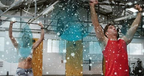 Winter workout partners training on pull-up rig with festive snow overlay in warehouse gym