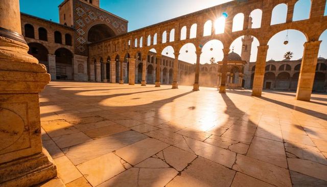 Golden morning sun casting long shadows across historic two-tier arcade and domed courtyard