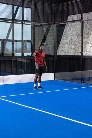 Athlete standing on blue padel court holding racket in indoor urban sports arena