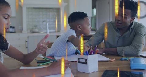 Father leaning forward engaging son in homework at kitchen table with daughter drawing