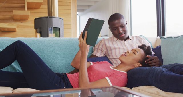 Image of happy african american couple sitting on sofa and reading together. Love, relationship and spending quality time together concept.