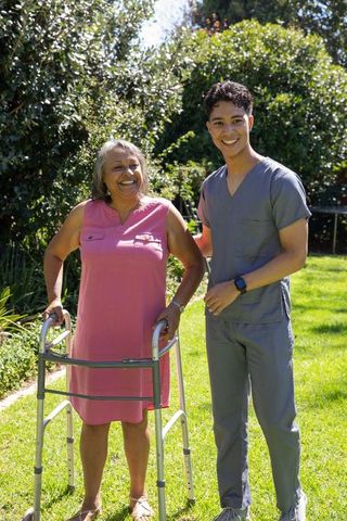 Senior Woman Deambulating With Caregiver Outdoors On Sunny Day