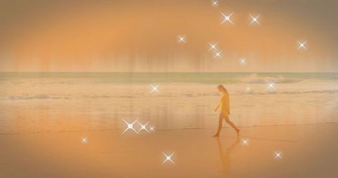 Woman walking on golden beach at sunset with sparkling star reflections and calm waves