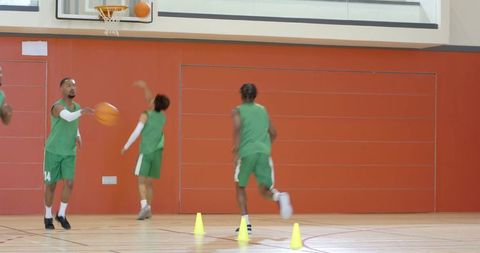 Diverse basketball teammates practicing cone drills and shooting layups in indoor court