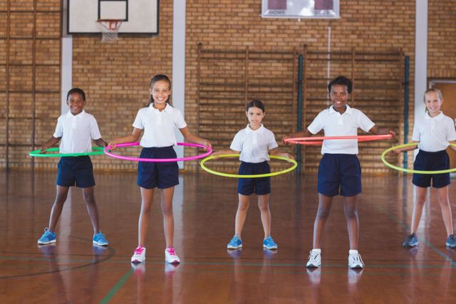 Children are engaging in a fun physical activity with hula hoops in a school gym. This image can be used for educational materials, promoting physical education, fitness programs for kids, or advertisements for school sports equipment.