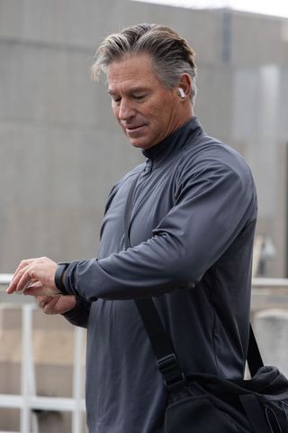 Middle-aged man checking smartwatch on urban rooftop wearing earbuds and gym duffel
