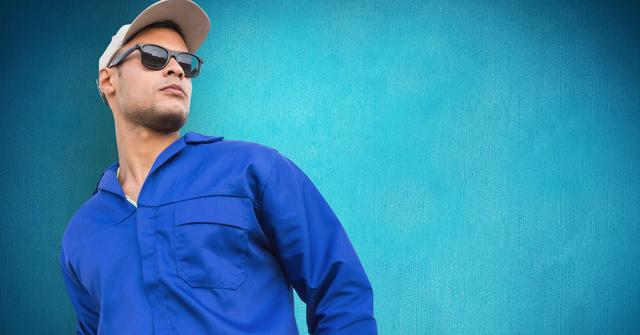 Serviceman dressed in a blue uniform and wearing sunglasses, looking sideways with a confident expression against a bright blue background. This image is perfect for advertising fashion workwear, promoting professional maintenance or repair services, and illustrating job opportunities in industries requiring uniforms.