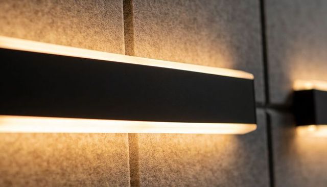 Minimalist Matte Black Wall Sconce Casting Warm Amber Glow on Gray Felt Panels