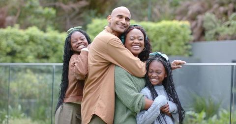 African American family hugging and laughing on balcony with glass railing and garden