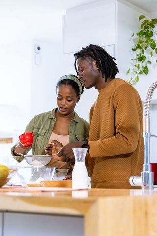 African american couple baking together in modern kitchen sifting flour and mixing batter