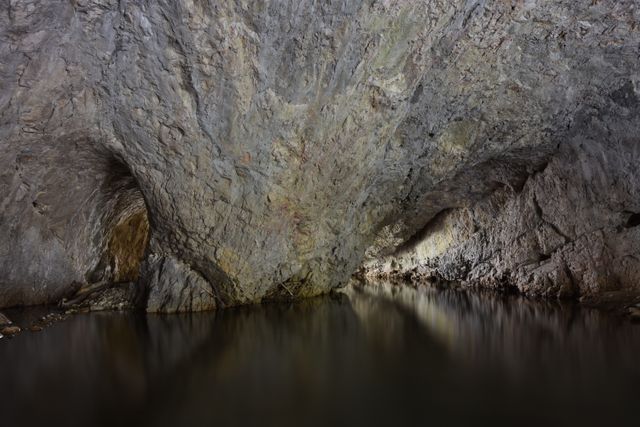 Image depicts underground cave with clear water reflecting rugged rock walls, creating serene and eerie ambience. Perfect for illustrating geological features, nature documentaries, adventurous settings, or artistic backgrounds.