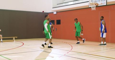 Competitive indoor basketball players in green and blue jerseys executing fast court teamwork