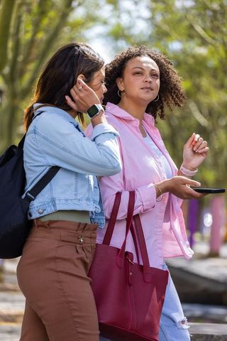 African american friends walking in park chatting and using smartphone carrying red tote
