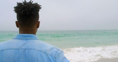 Man Gazing at Ocean Waves on Tranquil Beach Day