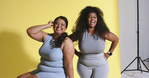 Plus-size women laughing and posing in matching grey activewear on bright yellow backdrop