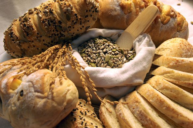 Assorted freshly baked bread loaves surrounding a small cloth bag filled with various seeds. This image captures a variety of bread types, showcasing textures and toppings like sesame and sunflower seeds. Ideal for use in bakery advertisements, cooking blogs, recipe books, or nutritional articles emphasizing healthy eating and homemade cuisine.