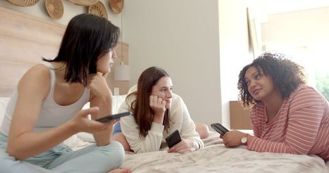 Diverse Friends Relaxing and Chatting with Smartphones in Cozy Bedroom