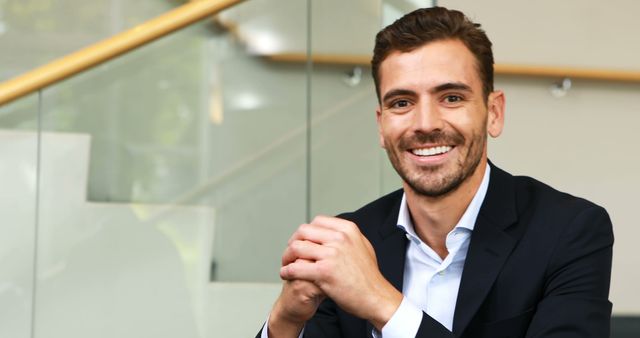 Confident businessman wearing suit smiling at camera in modern office environment. Ideal for business promotions, corporate websites, and professional profiles.